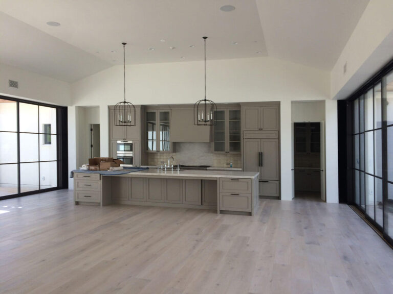 modern-kitchen-with-large-island-and-glass-doors Spacious modern kitchen featuring a large island, pendant lights, and glass sliding doors.